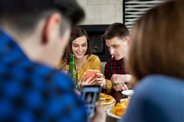 Group of friends in a cafe with pizza and beer having fun. The girl shows the guy a funny photo on...