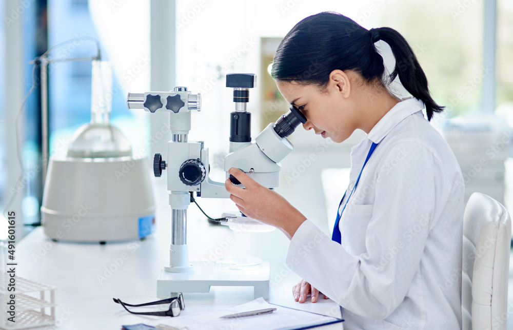 Poster the closer she looks, the closer the answer. shot of a young scientist using a microscope in a labor