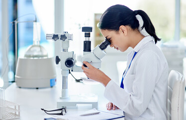 The closer she looks, the closer the answer. Shot of a young scientist using a microscope in a...