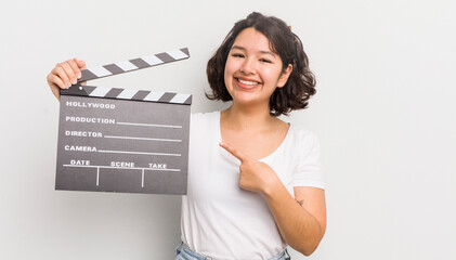 pretty hispanic girl smiling cheerfully, feeling happy and pointing to the side. cinema concept - obrazy, fototapety, plakaty
