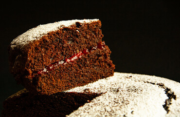 Ciasto czekoladowe brownie z dżemem truskawkowym i cukrem pudrem na czarnym tle.