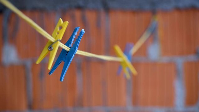 Laundry pegs clothes pins attached on launtry cord white swinging in wind against blurred wall of blocks in selective focus