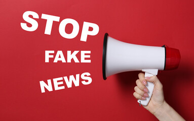 Female hand with megaphone and text STOP FAKE NEWS on red background