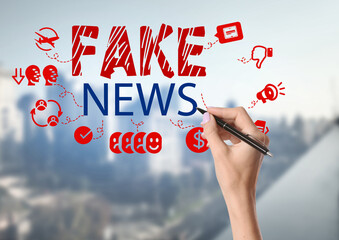 Hand of woman with pen writing text FAKE NEWS on glass