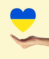 Female hand with heart in colors of Ukrainian flag on light background. War in Ukraine