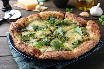 Delicious pizza with pesto, cheese and arugula on wooden table, closeup
