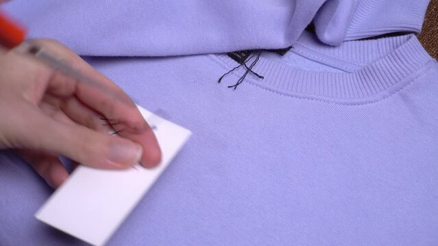 The girl's hands with scissors remove the price tag from the purple sweater. A woman after shopping. Something new. I'm buying clothes.