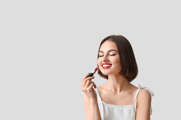 Happy woman with closed eyes holding red lipstick on light background