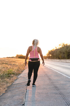 African American Woman On Her Back Walking On The Side Of The Road In Sportswear. 