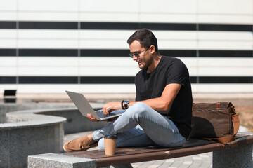 Handsome man using laptop on bench outdoors