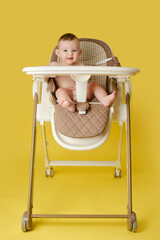 Happy baby sits on a high chair for feeding children, studio yellow background. Smiling child boy...