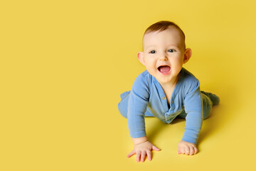 Happy toddler baby plays laughing on studio yellow background. Funny child boy crawling and smiling, copy space