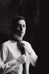 Morning of a stylish groom, man, in a black suit and tie, his preparations at the hotel, in a photo studio, fastening buttons and jacket, portraits