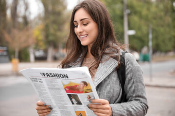 Beautiful young woman reading newspaper on city street
