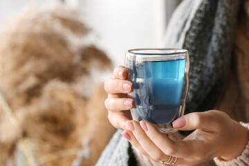 Woman with cup of tasty blue tea at home, closeup