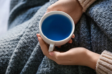 Woman with cup of tasty blue tea at home, closeup