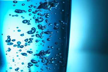 Glass of clear water with bubbles on blue background, closeup