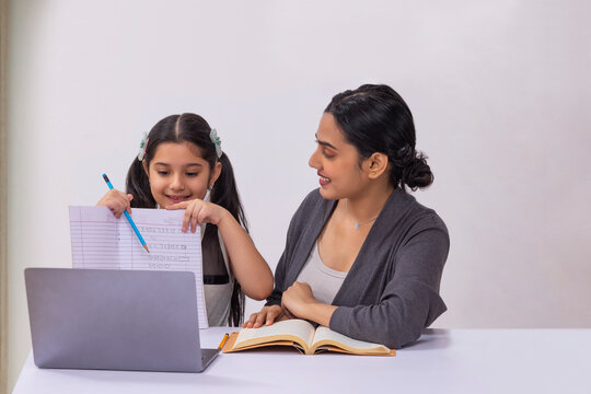 Girl submitting homework through online class using laptop and mother sitting beside