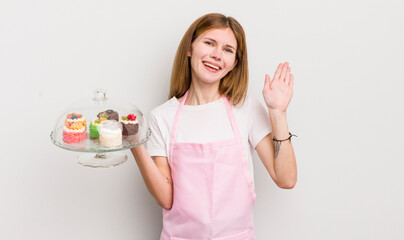 redhead pretty girl smiling happily, waving hand, welcoming and greeting you. home made cakes concept