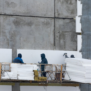 Square close-up photo of workers insulating the facade of the building.