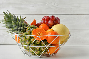 Basket with juicy fruits on white wooden background