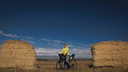 The man travel on mixed terrain cycle touring with bikepacking. The traveler journey with bicycle bags. Sport bikepacking, bike, sportswear in green black colors. Mountain snow capped, stone arch.