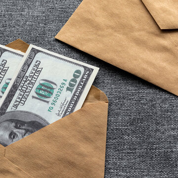 Concept on the topic of collecting money to pay taxes and debts. A square photo of American hundred-dollar bills in a craft paper envelope.