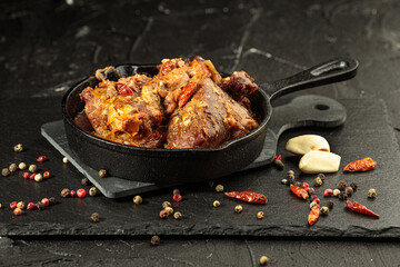 Pork stew in frying pan with species on black background, close up view
