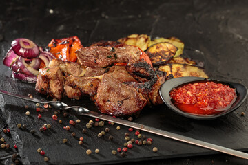 Shashlik or shish kebab prepared on barbecue grill over hot charcoal with grilled vegetables and hot sauce. close up view.