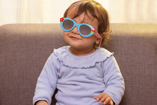 Portrait of a cute baby wearing sunglass while sitting on sofa in living room