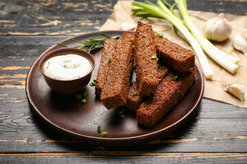Plate with tasty croutons and sauce on black wooden background