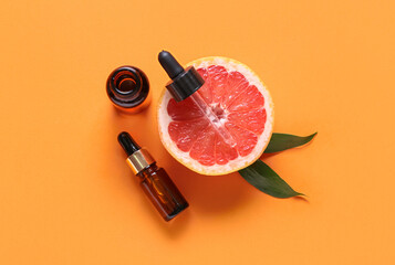 Bottles with essential oil and half of grapefruit on color background