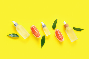 Composition with bottles of essential oil, grapefruit slices and plant leaves on yellow background