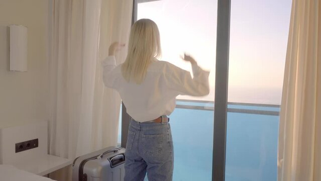 a young woman enters the room with a suitcase, opens a lace curtain, raises her hands, standing in a luxurious apartment, looking around the space, feeling happy, a tourist trip, vacation,