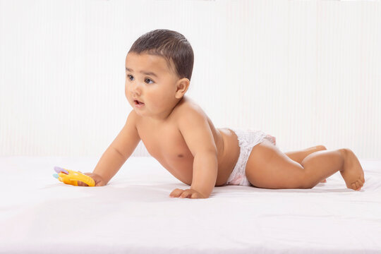 Cute baby in diaper crawling on bed with toy