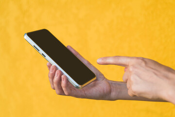 Finger in front of the phone in the girl's hand. Against the background of a yellow facade made of decorative plaster.