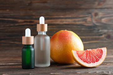 Bottles of essential oil and ripe grapefruit on wooden background