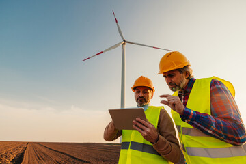 Electricity maintenance engineers working on the field at a wind turbine