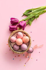 Basket with painted Easter eggs and tulip flowers on pink background