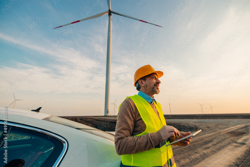 Wall mural Smiling engineer standing by car on a wind farm