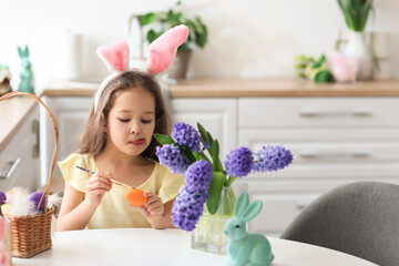 Cute little girl with bunny ears painting Easter egg in kitchen at home - obrazy, fototapety, plakaty
