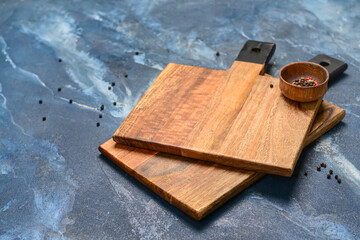 Wooden cutting boards and bowl with peppercorn on blue background