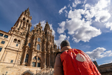 pilgrim in Obradoiro square looking the Santiago de Compostela cathedral after finishing the Camino de Santiago  , Galicia, Spain ; focus in background - obrazy, fototapety, plakaty
