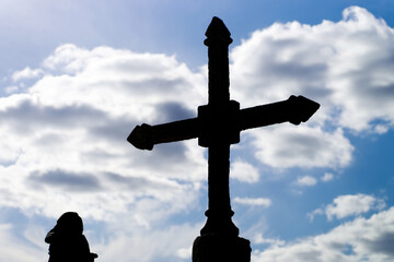 stone crosses and women in silhouette with blue sky and clouds in background