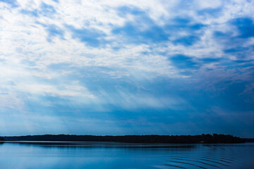 The rays of God in the river landscape. The sun's rays shine through the clouds over the water surface and the shore. Copy space
