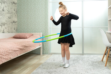 Fototapeta na wymiar A child spins a hoop at home in the living room. Little girl with a dancing black dress twists a hoop at home in the living room
