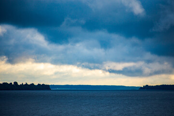 Fototapeta premium River landscape. Calm water and dramatic sky with clouds. Trees grow on the nearest shore. There is a copy space