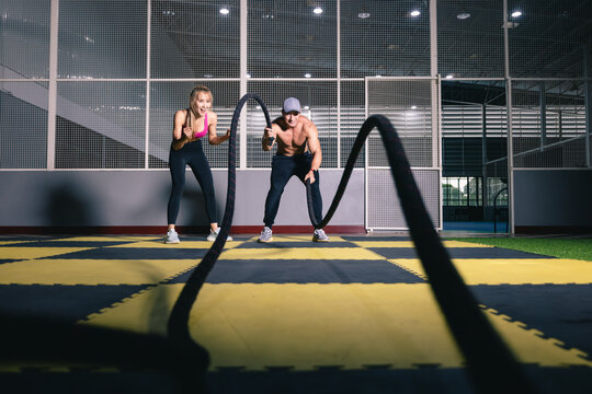 Athletic young man and asian woman doing with encourage some cross training exercises with a battle rope.