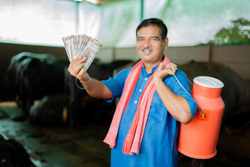 focus on notes, Milk production dairy famer with milk container in hand showing stack of money by...