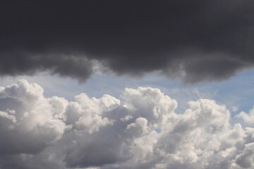 White and dark grey cumulus clouds on blue sky, opposing each other dramatically. Cloudscape...